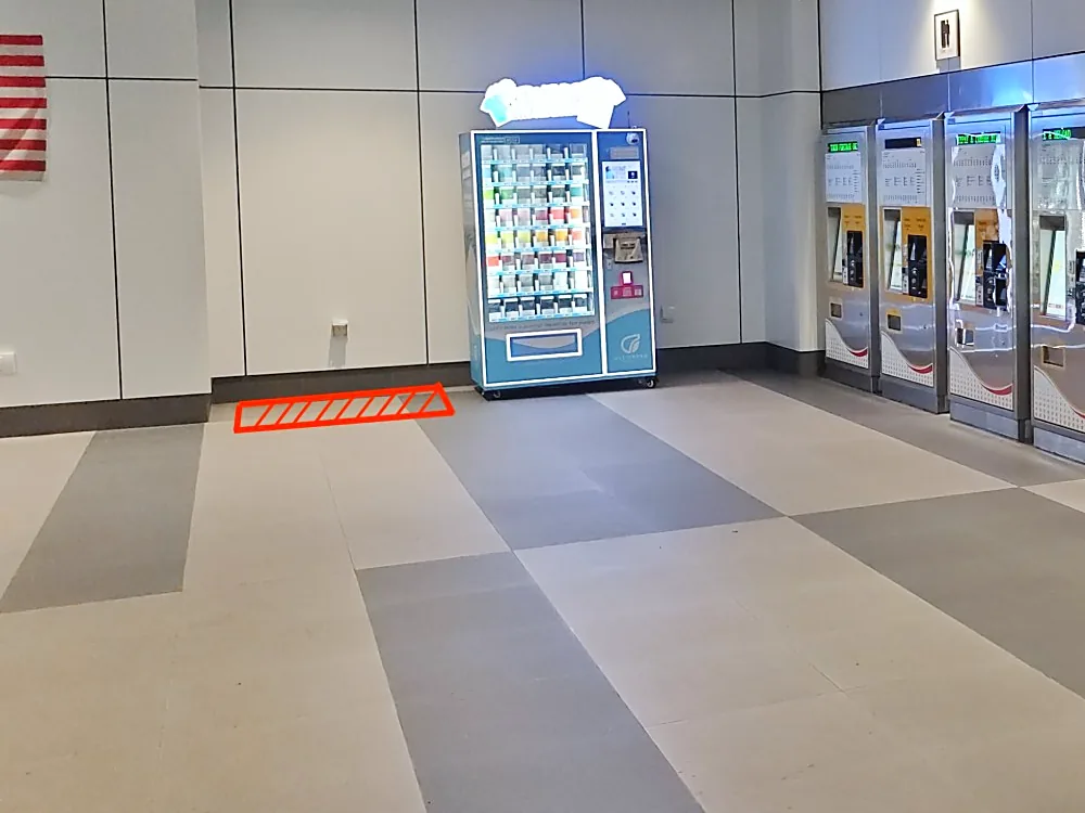A train station concourse with a red outline on the floor next to a vending machine marking the space to rent