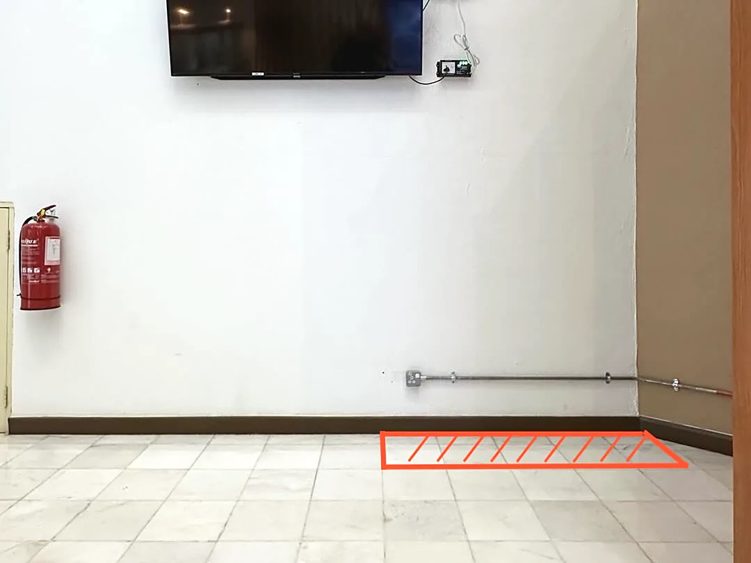 A bare wall with a power socket and a red outline on the tiled floor marking the space to rent